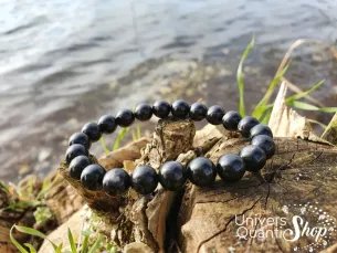 hypersthène bracelet de lithothérapie 08mm au bord d'un tronc d'arbre près de l'eau