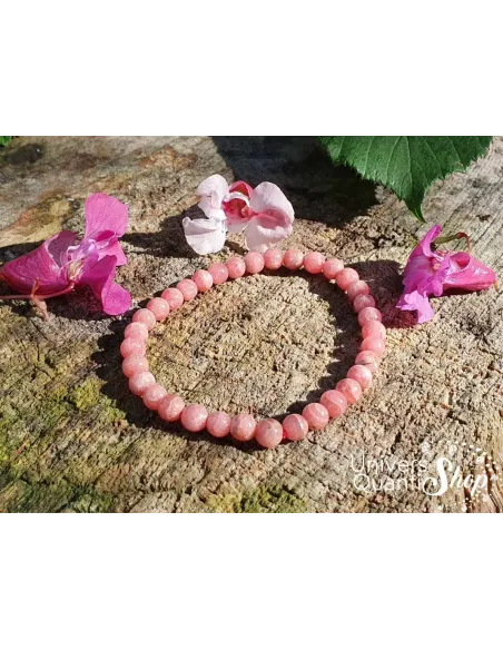 rhodochrosite signification bracelet 5mm posé sur un rocher avec des fleurs roses