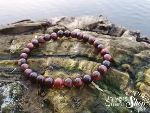 oeil de taureau bracelet pierre d'action 6mm posé sur un morceau de bois au bord de l'eau