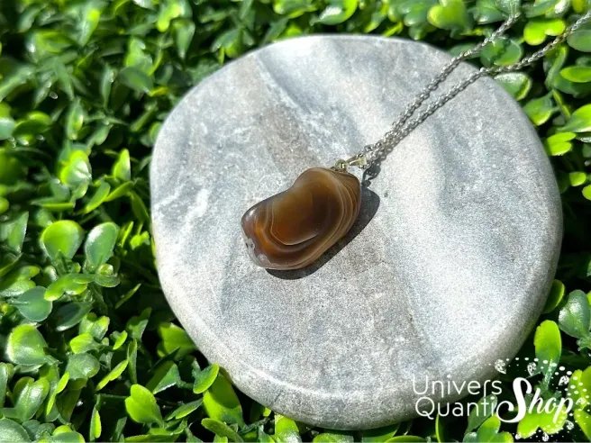 agate botswana vertus pendentif lithothérapie posé sur un bloc en marbre sur l'herbe