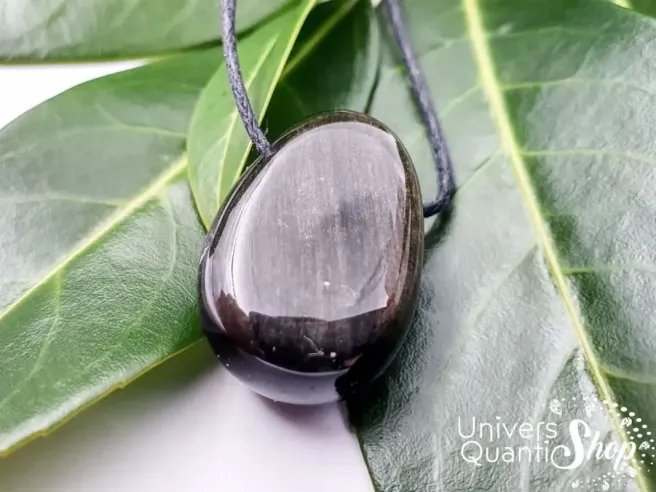 pendentif pierre obsidienne dorée posé sur des feuilles vertes - univers quantic shop