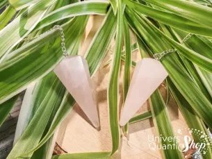 pendule divinatoire quartz rose pointe facettée posé sur des feuilles vertes