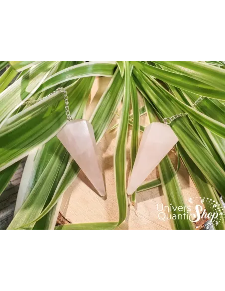 pendule divinatoire quartz rose pointe facettée posé sur des feuilles vertes