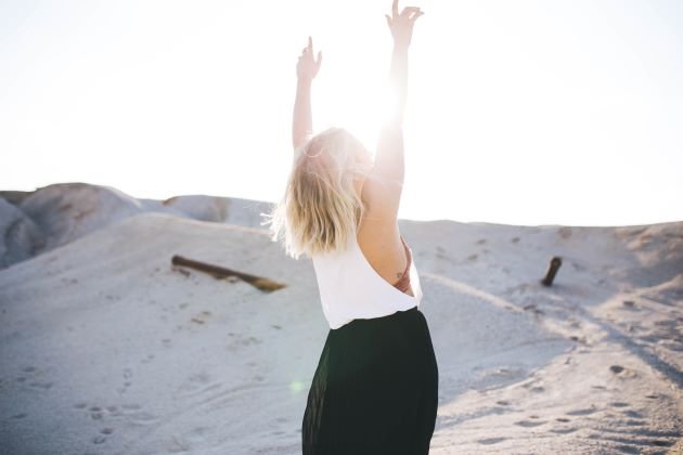 femme qui lève les mains haut en l'air avec le soleil et le sable en fond sortir de la culpabilité