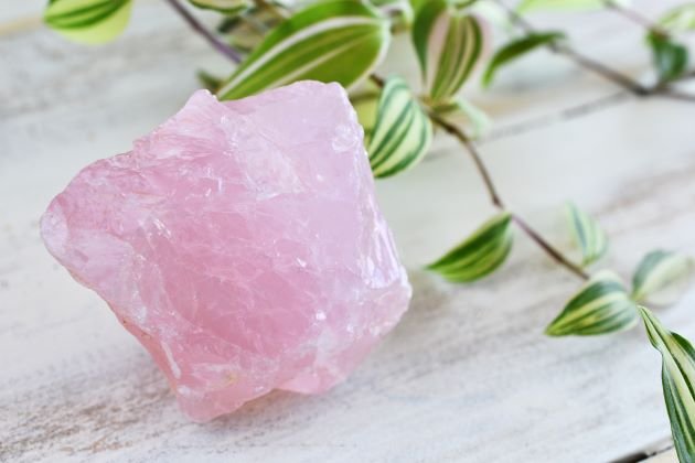 quartz rose pierre brute sur un fond blanc avec branche de feuilles pour amener réconfort en période de deuil
