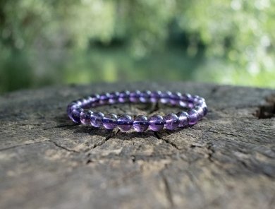 bracelet améthyste violet posé sur un tronc d'arbre en nature