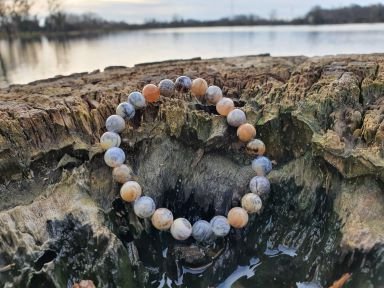 bracelet agate dendritique 8 mm posé sur un rocher au bord d'un lac